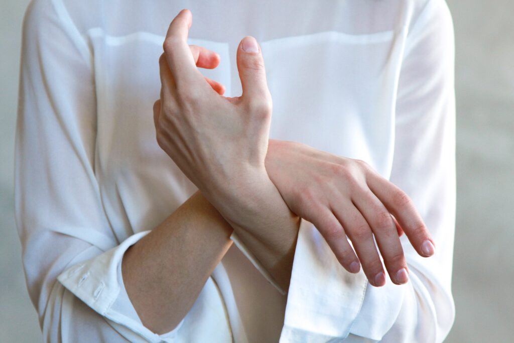 Moteris baltais marškiniais sukryžiavusi rankas